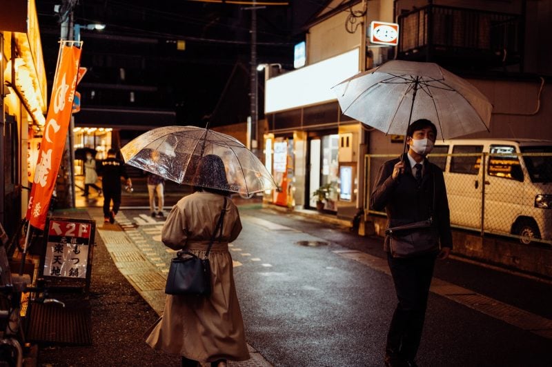 People walking in the rain at night on a street in Japan.