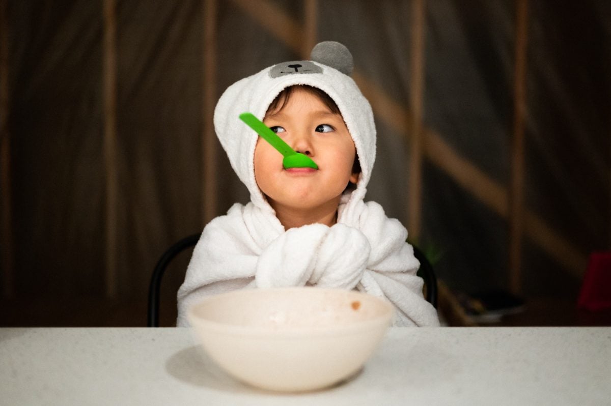 Boy eating cereal with a spoon in his mouth.