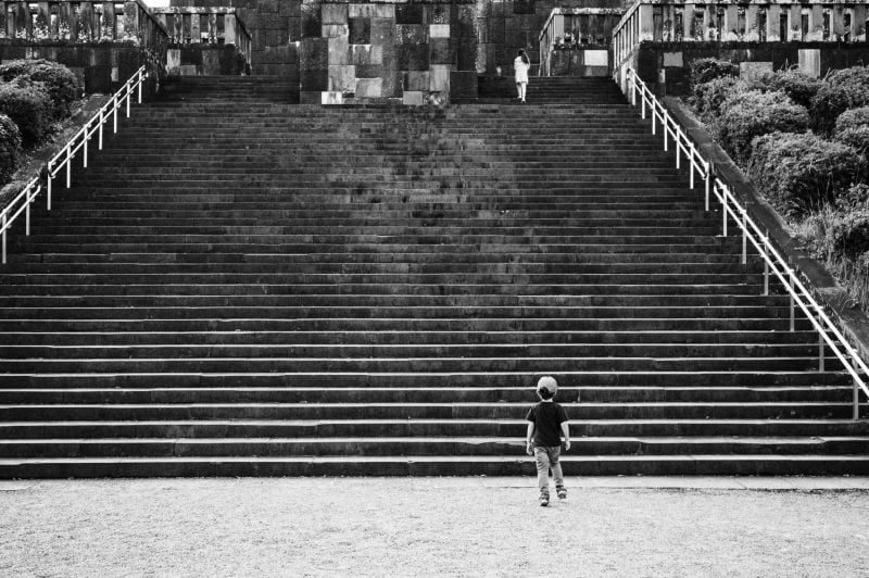 Boy stands at the base of stairs of a Japanese Temple